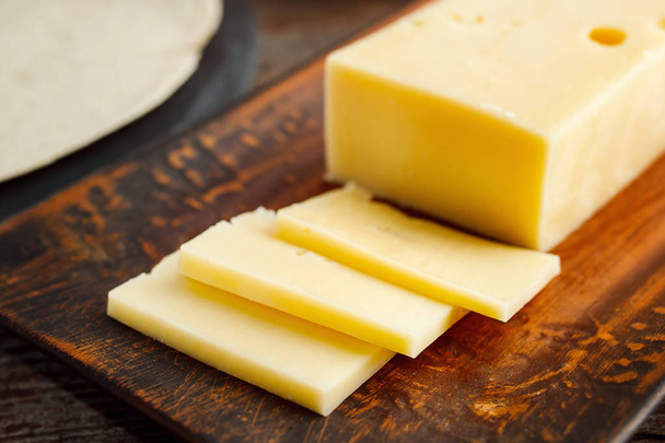 Κόψτε τα κομμάτια του τυριού σε μια πήλινη πλάκα σε ένα ξύλινο τραπέζι. - Φωτογραφία, εικόνα