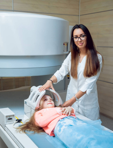 Doctora joven y paciente niña en sala de resonancia magnética en el hospital. Equipos médicos
.  - Foto, imagen