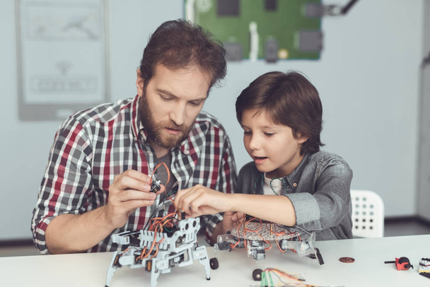 A man helps a boy with a robot assembly. The boy looks carefully as a man collects a robot - Fotoğraf, Görsel