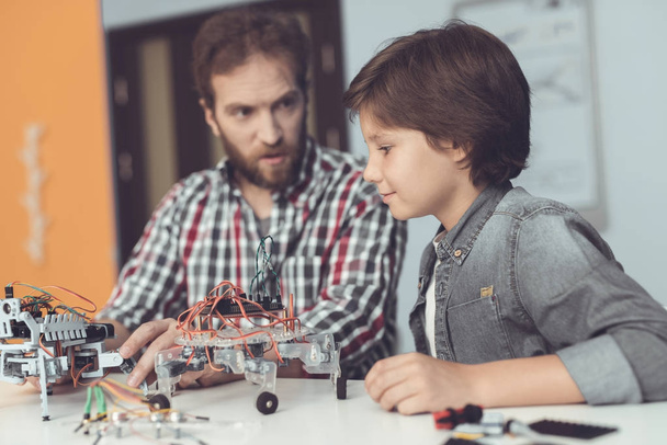 A man helps a boy with a robot assembly. The boy looks carefully as a man collects a robot - Foto, Imagem