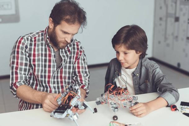 A man helps a boy with a robot assembly. The boy looks carefully as a man collects a robot - Fotoğraf, Görsel