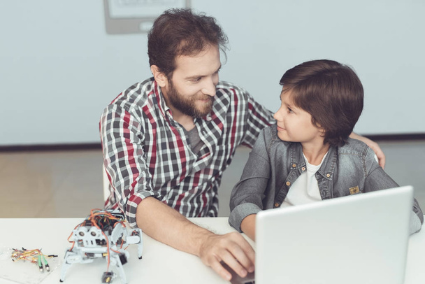 A man helps a boy with a robot assembly. They sit in front of the laptop and are preparing to program the robot - Фото, зображення