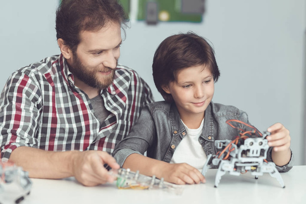 A man helps a boy with a robot assembly. A man watches as the boy finishes assembling the robot - Фото, изображение