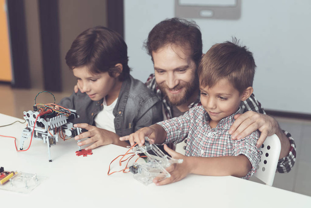 A man and two boys construct a robot. The man helps the boys with the assembly - Фото, изображение