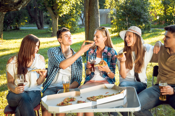 Cheerful friends on picnic in park eating pizza. - Foto, afbeelding