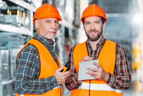 two male workers holding walkie talkie and notepad in storehouse - Photo, Image