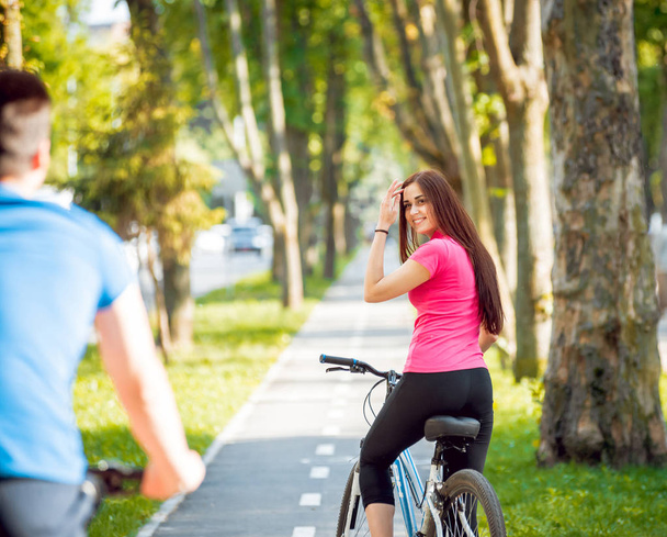 Молода біла пара катається на зеленій велосипедній доріжці в сонячний день
 - Фото, зображення