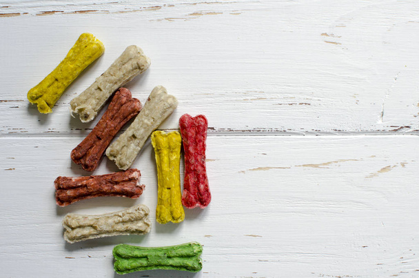 köstliche Kauknochen für Hunde mit unterschiedlichem Geschmack auf weißem Holzhintergrund - Foto, Bild