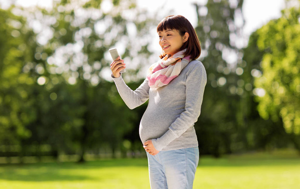 happy pregnant asian woman taking selfie at park - Fotó, kép