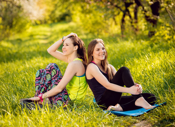 Two young girls practicing yoga in the park and having fun - Фото, изображение