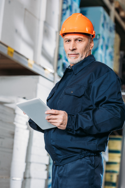 trabajador masculino senior en casco con tableta digital en stock de envío
 - Foto, Imagen