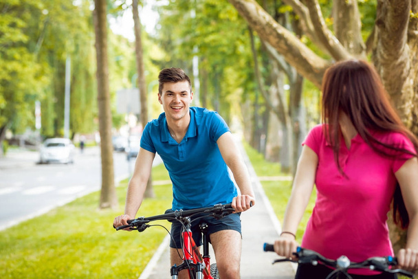 Young caucasian couple cycling on green bicycle lane in sunny day - Φωτογραφία, εικόνα
