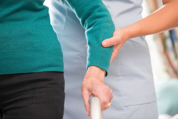Senior Woman's Hands On Walking Frame With Care Worker In Backgr - Photo, Image