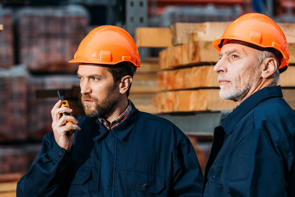 budowniczowie w twardych kapeluszach pracujący z walkie talkie na zewnątrz przy budowie - Zdjęcie, obraz