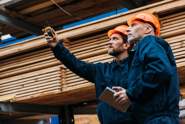 constructores en cascos apuntando con walkie talkie en la construcción
 - Foto, Imagen