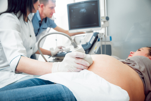 Female doctor and young pregnant woman patient with husband. Ultrasound equipment. Diagnostics. Sonography. - Photo, Image