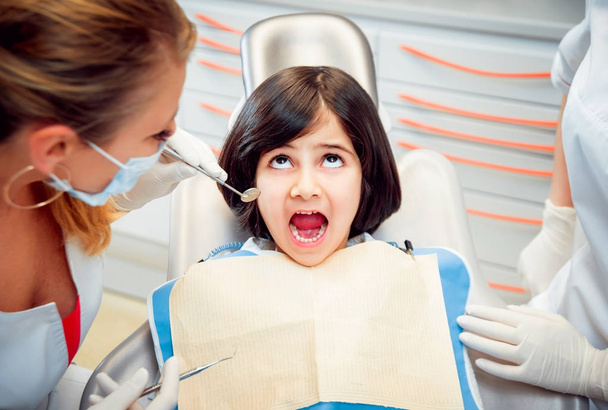 Little cheerful girl with bobbed dark hair in dental clinic with doctor and nurse - Foto, Imagen