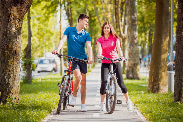 Jeune couple caucasien faisant du vélo sur une piste cyclable verte par temps ensoleillé
 - Photo, image