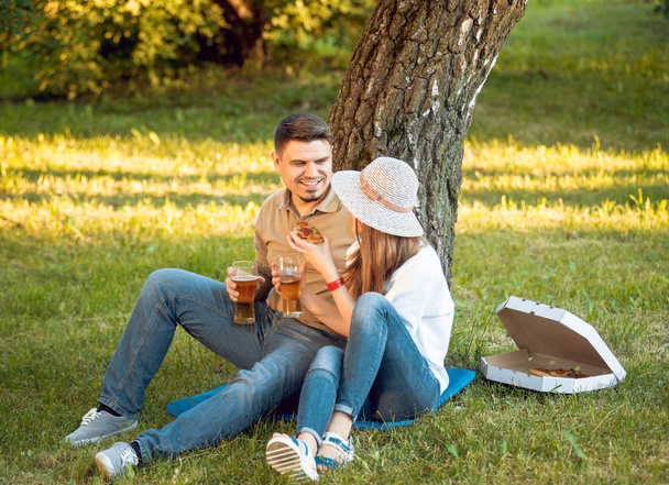 Happy couple on picnic in park. Eating pizza and drinking beer. - Fotoğraf, Görsel