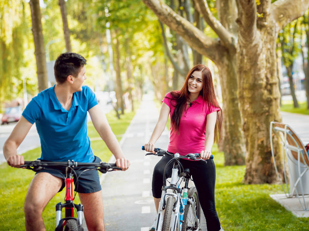 Young caucasian couple cycling on green bicycle lane in sunny day - 写真・画像