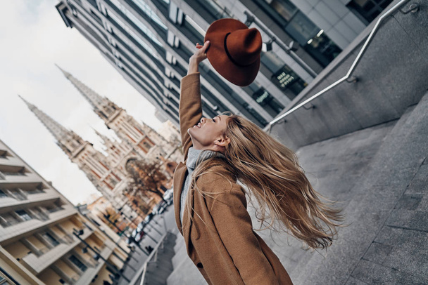 gorgeous blonde woman in city holding hat above head, catholic church on background - Zdjęcie, obraz