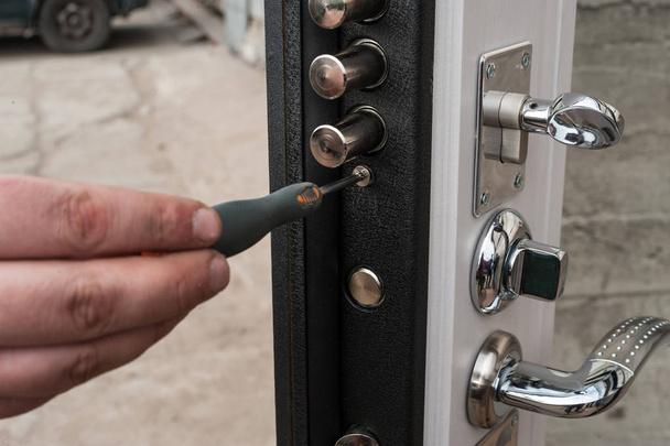 The carpenter installs a reliable burglar-resistant lock in the metal door. - Foto, immagini