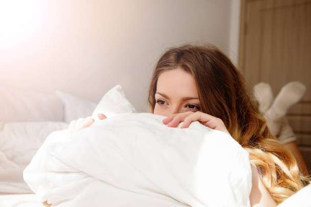 Muotokuva kaunis nuori tyttö sängyllä modernissa asunnossa aamulla. Kaunis nuori nainen avaa silmänsä ja näyttää tyytyväiseltä
 - Valokuva, kuva