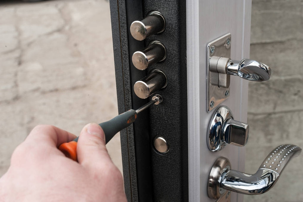 Ο ξυλουργός εγκαθιστά μια αξιόπιστη Αντιδιαρρηκτικά κλειδαριά στην πόρτα μεταλλική. - Φωτογραφία, εικόνα