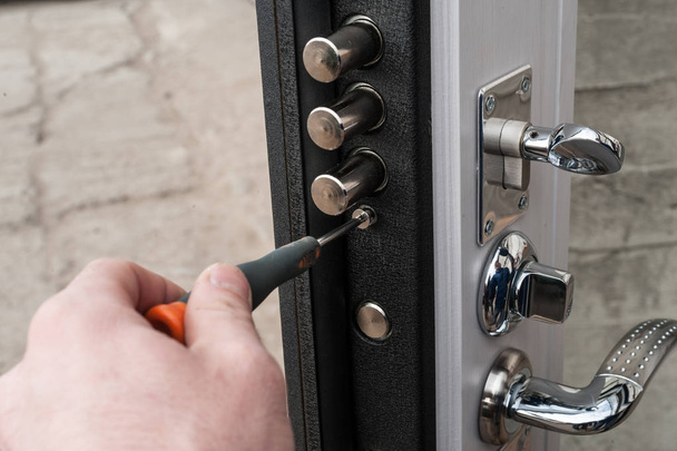 The carpenter installs a reliable burglar-resistant lock in the metal door. - Foto, afbeelding