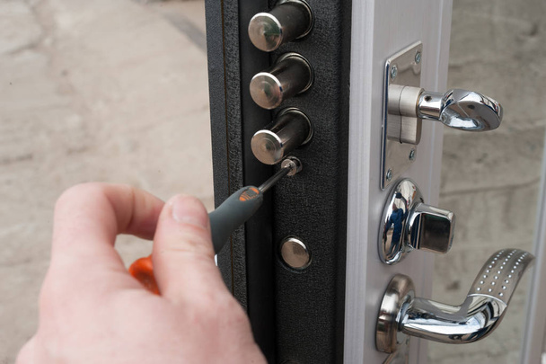 The carpenter installs a reliable burglar-resistant lock in the metal door. - Valokuva, kuva