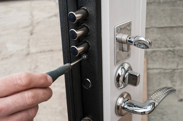 The carpenter installs a reliable burglar-resistant lock in the metal door. - Zdjęcie, obraz