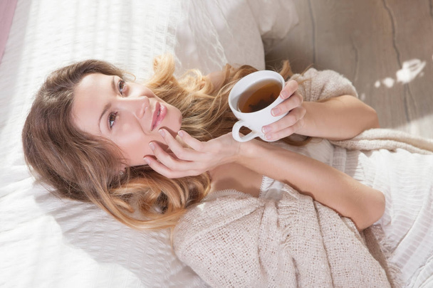 Closeup portrait of relaxing young woman enjoying coffee while sitting on floor near bed. Lazy morning in bed. - Φωτογραφία, εικόνα