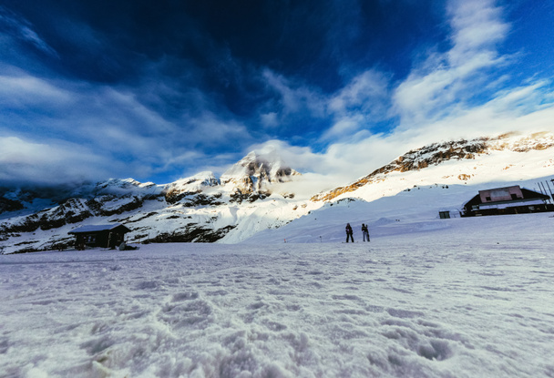 rauhallinen vuoristomaisema sinisen taivaan alla turistien kävellessä lumella, Itävalta
 - Valokuva, kuva