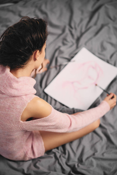 Meisje zit in haar bed en schilderen van een schilderij op de ochtend - Foto, afbeelding