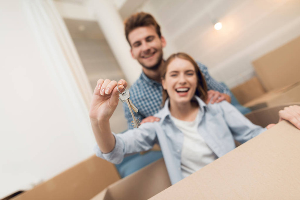 Young couple having fun while moving to new apartment. Moving newlyweds. Girl is sitting in a box. - Foto, Bild