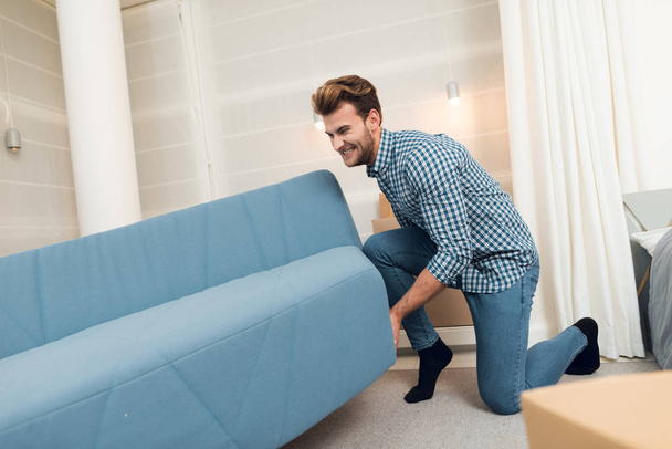 The guy moves the sofa while moving to a new home. The guy does a reshuffle in the room. - Фото, изображение