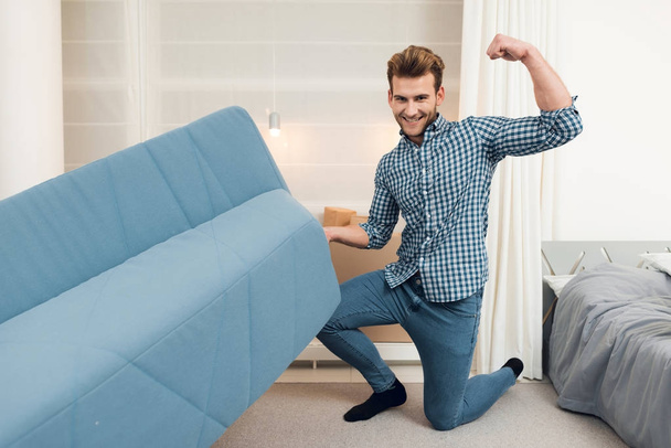 The guy moves the sofa while moving to a new home. The guy does a reshuffle in the room. - Photo, image