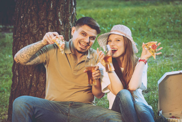 Happy couple on picnic in park eating pizza and drinking beer. - Φωτογραφία, εικόνα
