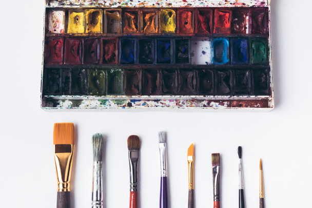 top view of well organized paint brushes and watercolor paints on white - Photo, Image