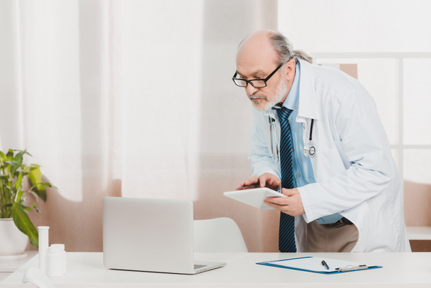Porträt des Oberarztes im weißen Kittel mit Tablet in der Hand am Arbeitsplatz in der Klinik - Foto, Bild