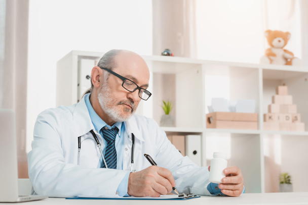 портрет зосередженого старшого лікаря, який робить нотатки на блокноті на робочому місці в клініці
 - Фото, зображення