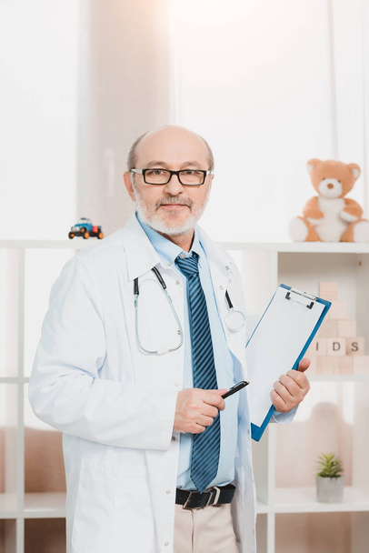 portrait of senior doctor in eyeglasses with stethoscope and notepad looking at camera - 写真・画像