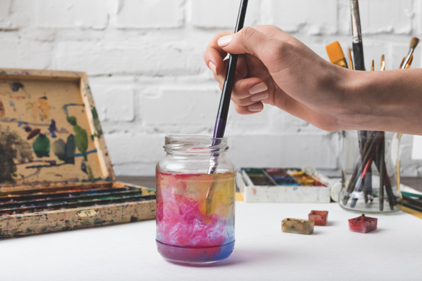 recortado tiro de artista poniendo pincel en frasco de vidrio con agua en el lugar de trabajo
 - Foto, Imagen