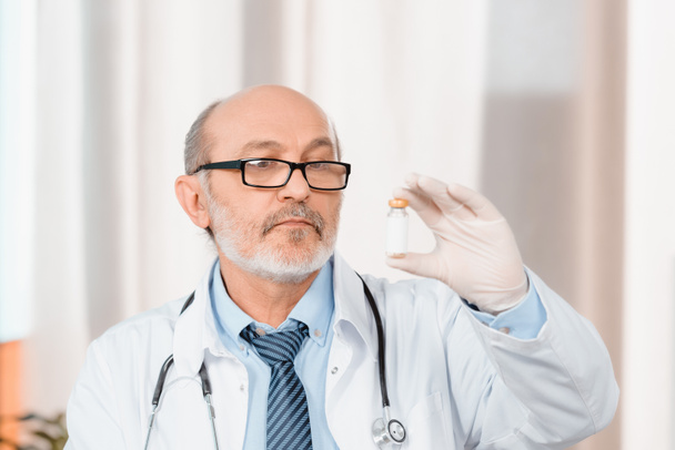 retrato de médico senior en anteojos y guantes médicos mirando medicamentos en la mano en la clínica
 - Foto, imagen