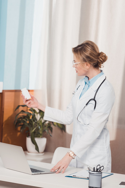 portret lekarza w białym płaszczu z lekami w ręku stojąc w miejscu pracy w klinice - Zdjęcie, obraz