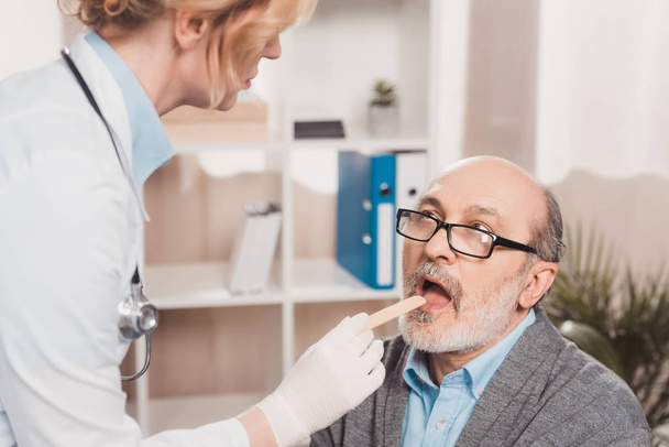 селективное внимание врача в медицинских перчатках, проверяющего горло пациента в клинике
 - Фото, изображение