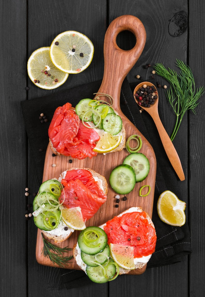Bruschetta with salmon and fresh cucumber on cutting board  - Photo, Image