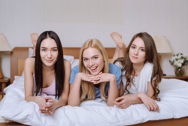 multicultural friends lying on bed and looking at camera - Foto, Imagen