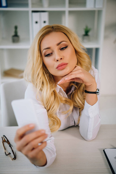 attractive businesswoman taking selfie at working place with smartphone - Photo, Image