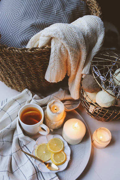Cozy winter morning at home. Hot tea with lemon, candles, knitted sweaters in basket and modern metallic interior details. Still life composition, danish hygge concept - Photo, image